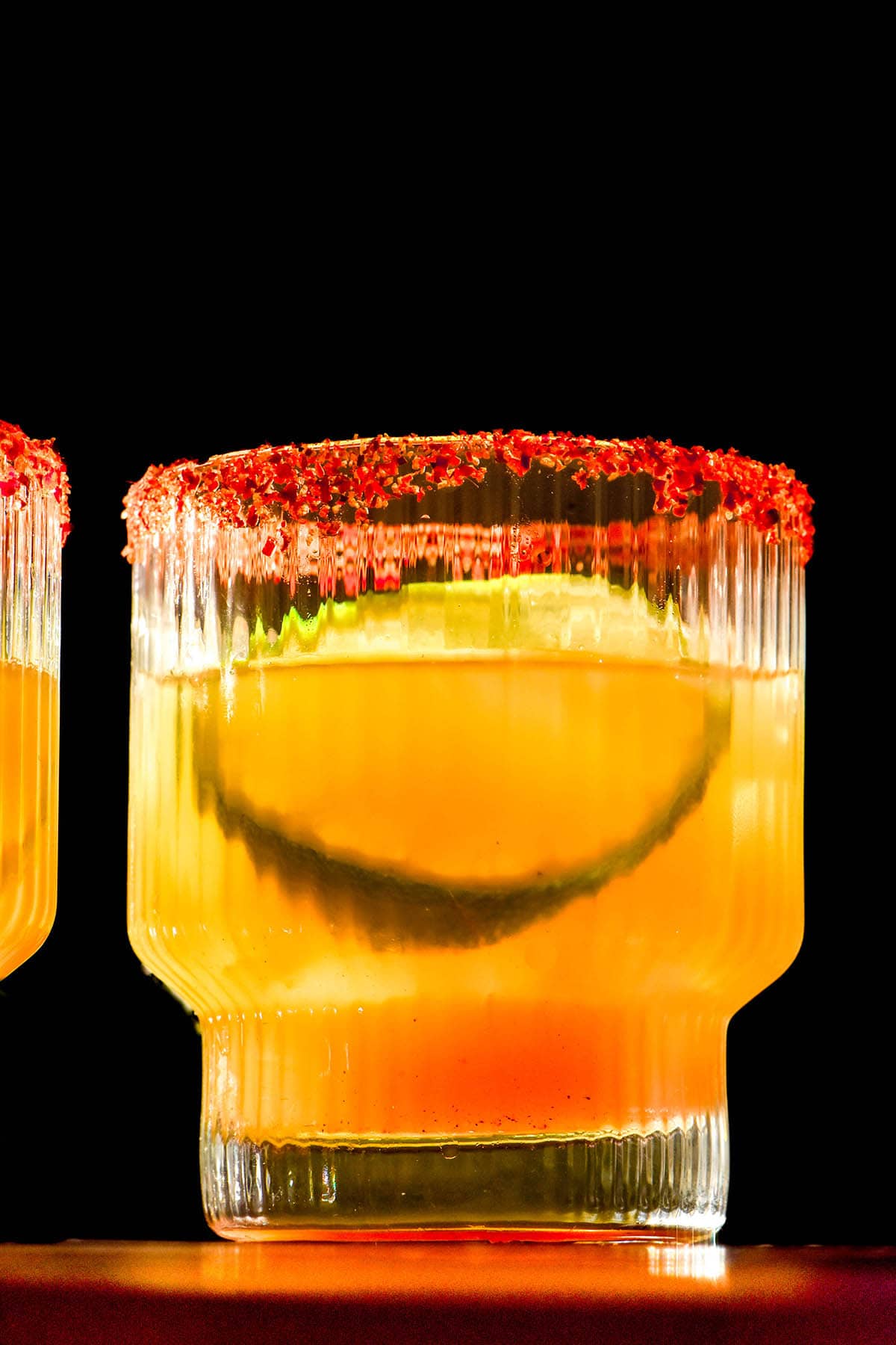 A dark and contrasted image of a non alcoholic margarita with a tajin rim against a black backdrop