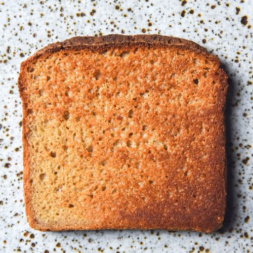 An aerial image of a slice of quinoa bread toast on a white speckled ceramic plate