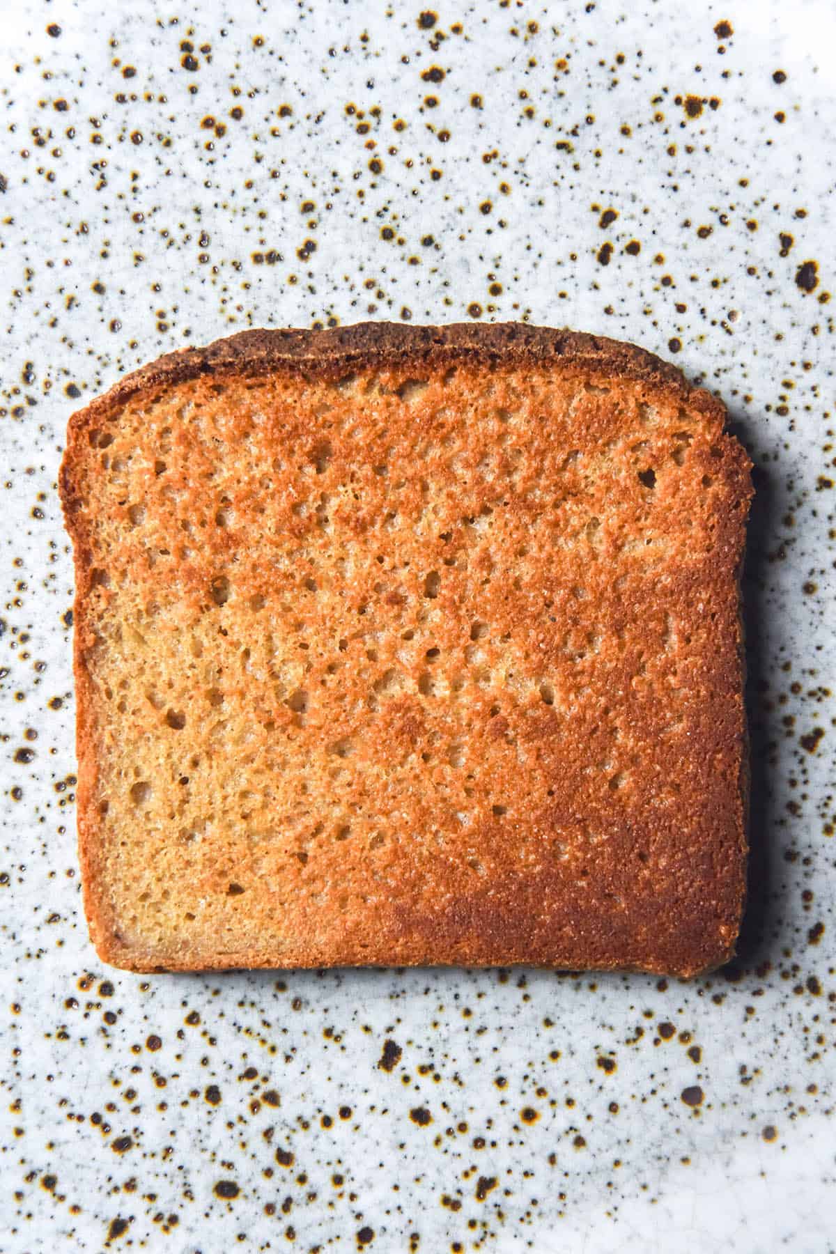 An aerial image of a slice of quinoa bread toast on a white speckled ceramic plate