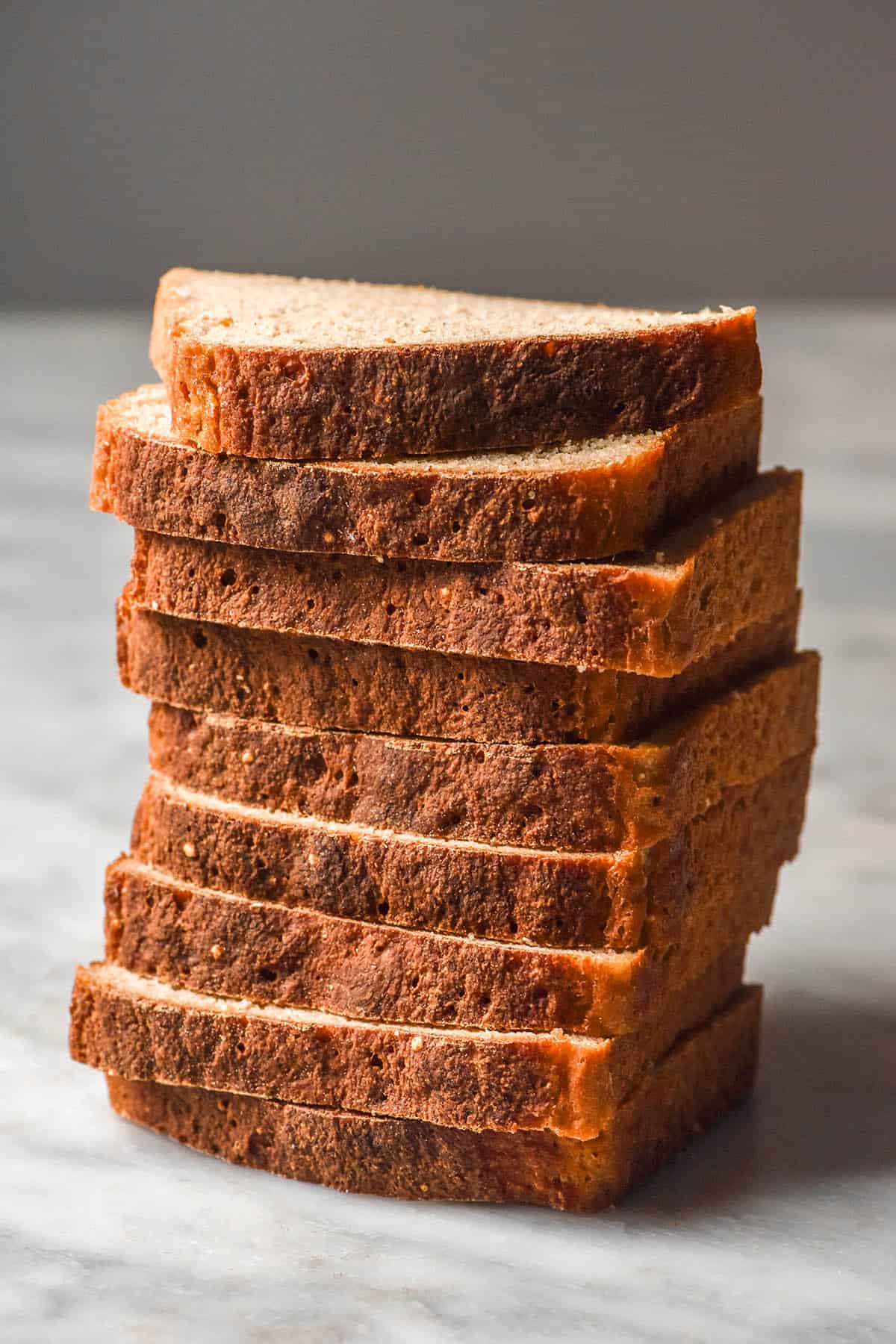 A side on image of a stack of sliced quinoa bread on a white marble table against a light backdrop