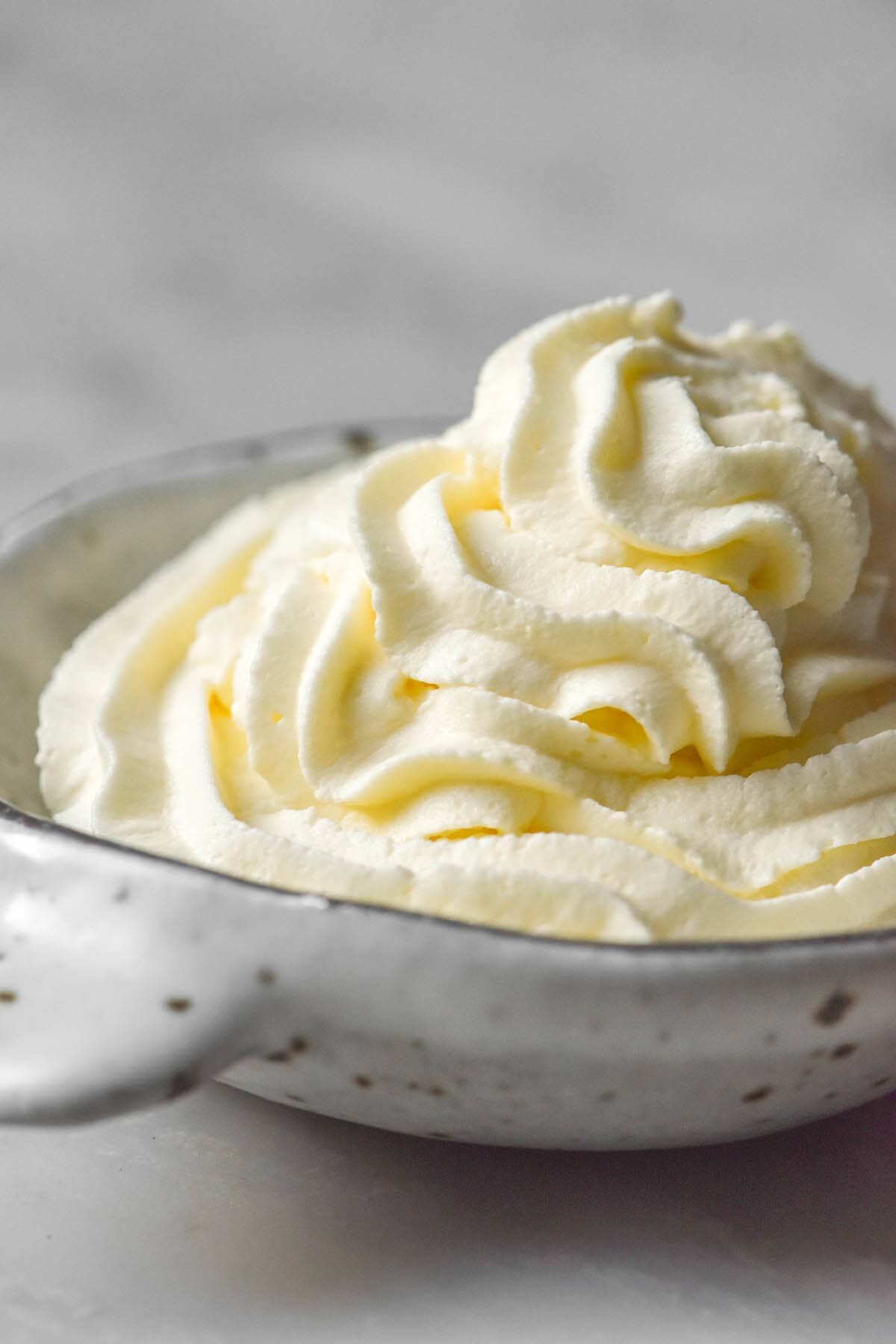 A side on image of a bowl of stabilised lactose free whipped cream using agar agar. The whipped cream sits in a small white ceramic bowl atop a white marble table