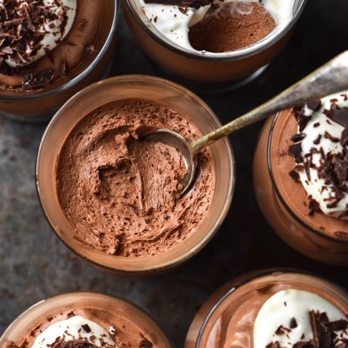 An aerial image of serving glasses filled with dairy free chocolate mousse topped with dairy free whipped cream and chocolate shards.