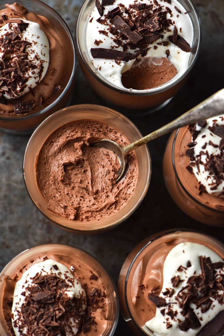 An aerial image of serving glasses filled with dairy free chocolate mousse topped with dairy free whipped cream and chocolate shards.