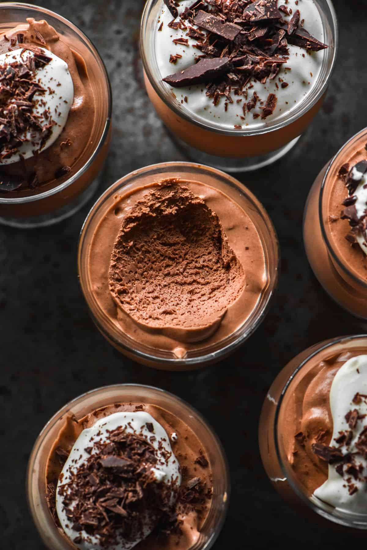 An aerial image of serving glasses filled with dairy free chocolate mousse topped with dairy free whipped cream and chocolate shards.