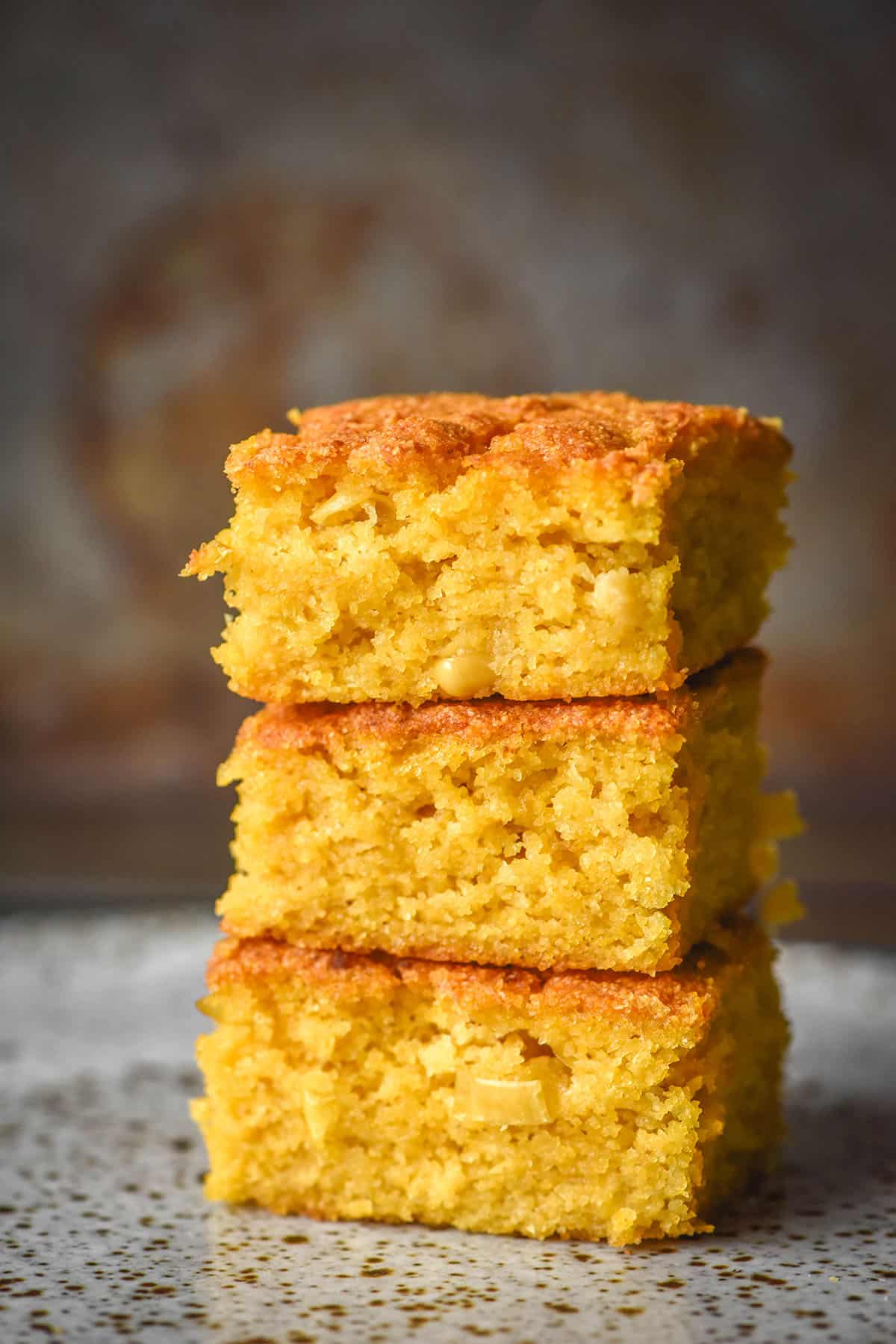 A side on image of a stack of gluten free cornbread slices on a white speckled ceramic plate against a dark backdrop