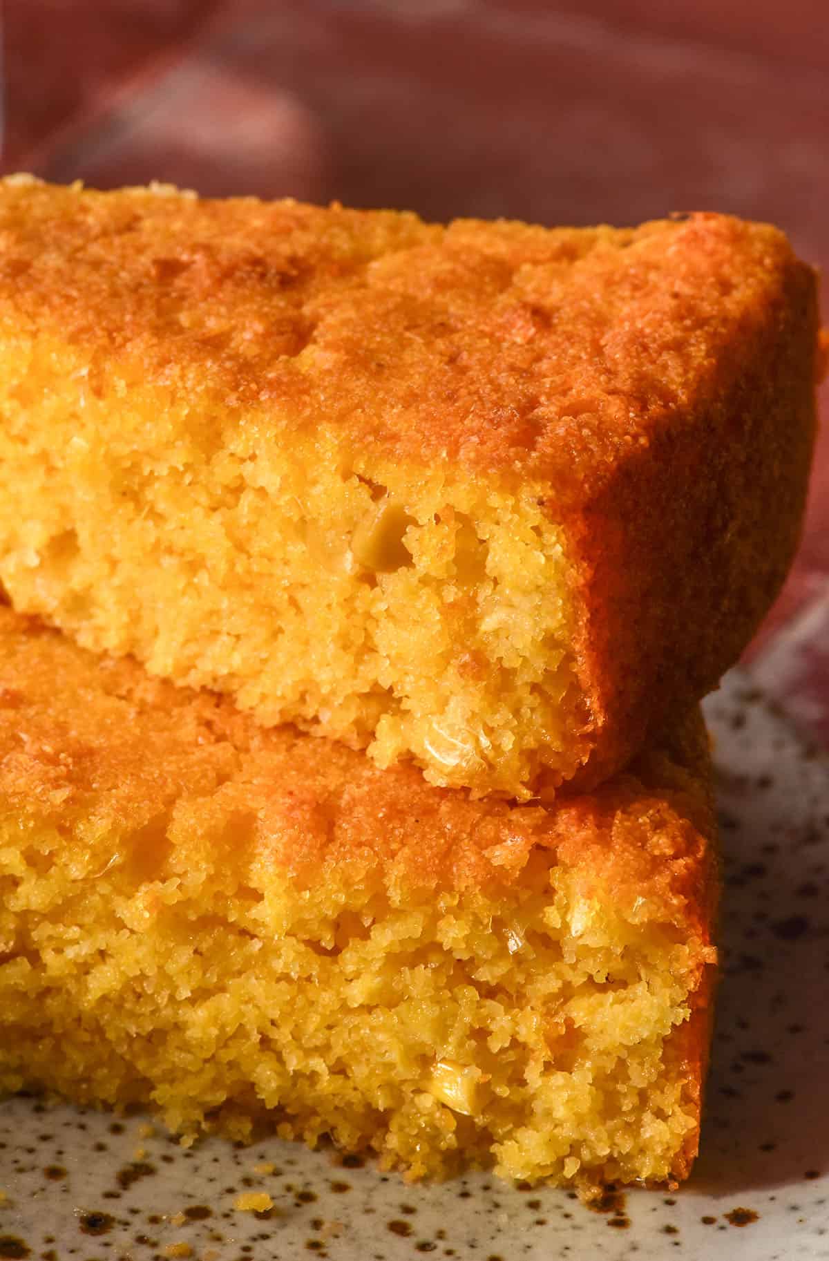 A side on image of two slices of gluten free cornbread stacked on top of a white speckled plate against a terracotta tile backdrop