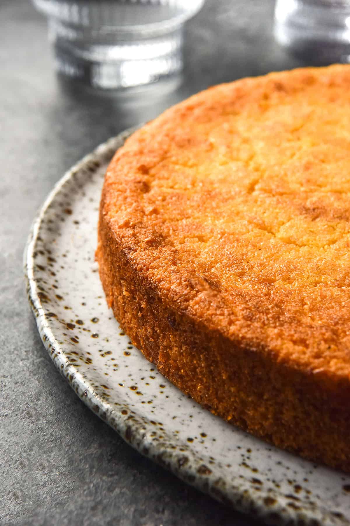 A side on image of a round gluten free cornbread on a white speckled ceramic plate against a dark blue backdrop