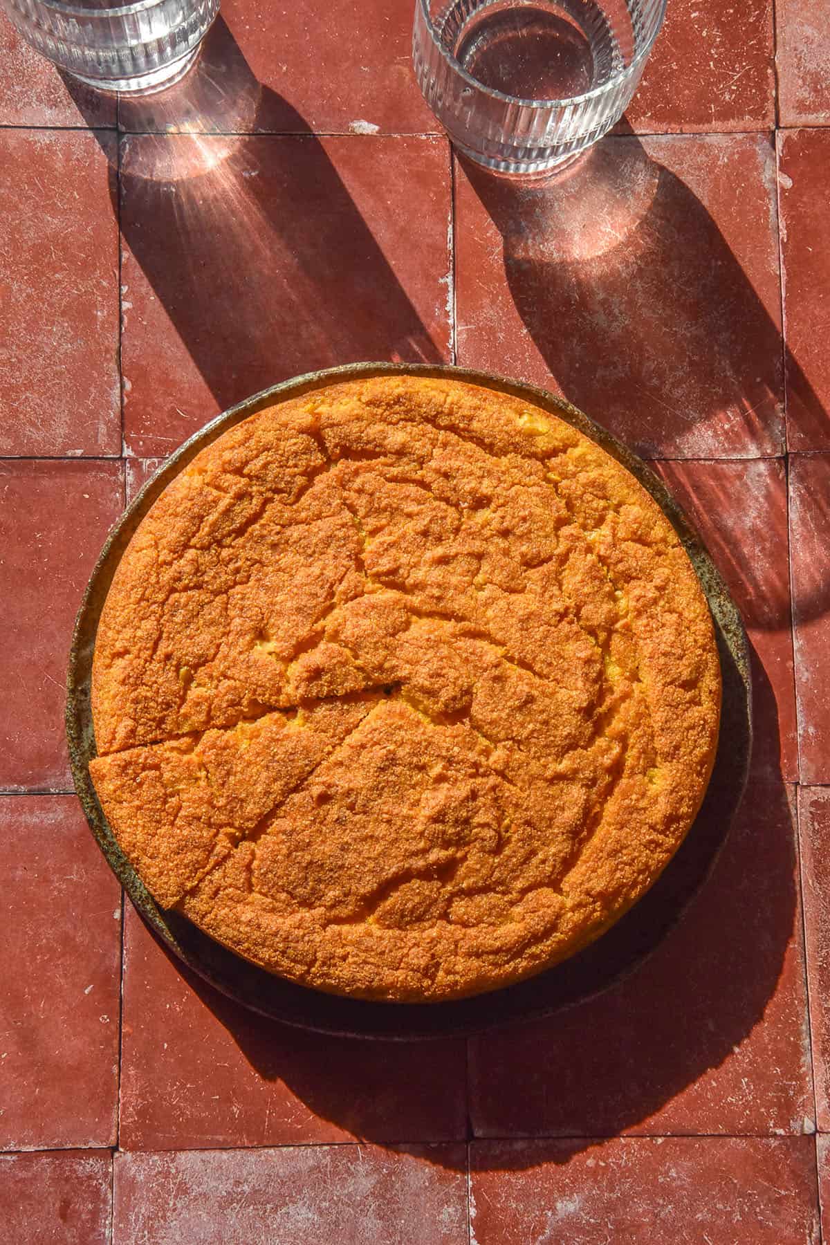 A sunlit aerial image of a gluten free cornbread on a terracotta tile backdrop