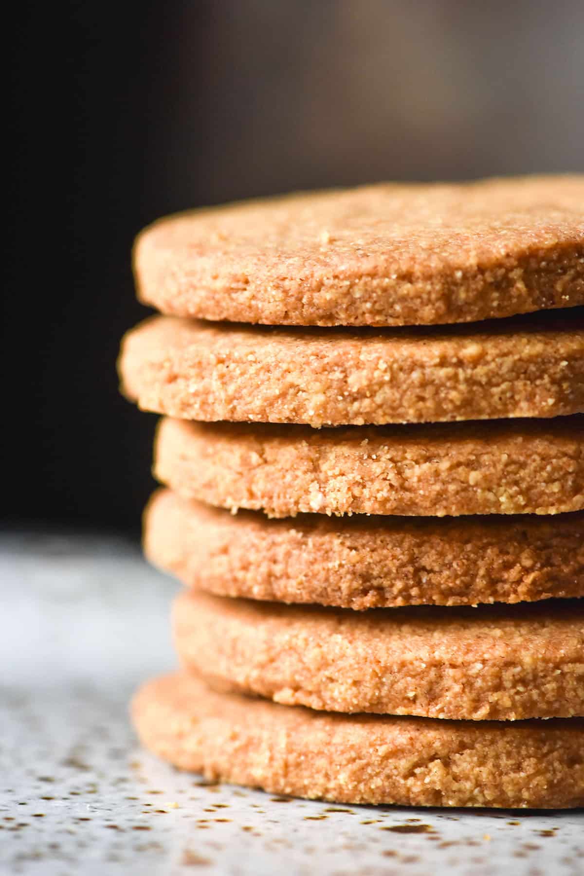 A side on macro image of a stack of gluten free digestive biscuits on a white speckled ceramic plate against a black backdrop