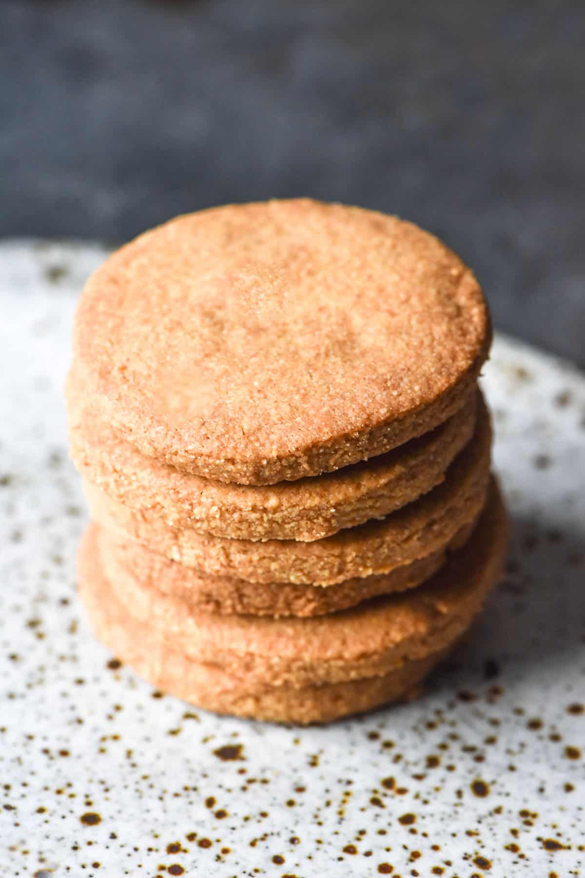 An elevated angle of a stack of gluten free digestive biscuits on a white speckled ceramic plate against a dark blue steel backdrop