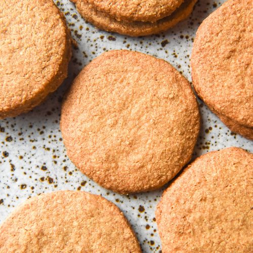 An aerial image of gluten free digestive biscuits arranged casually on a white speckled ceramic plate