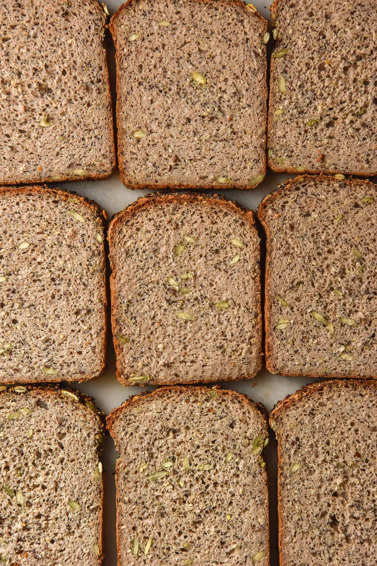 An aerial image of slices of seeded buckwheat bread arranged in a square atop a white marble table