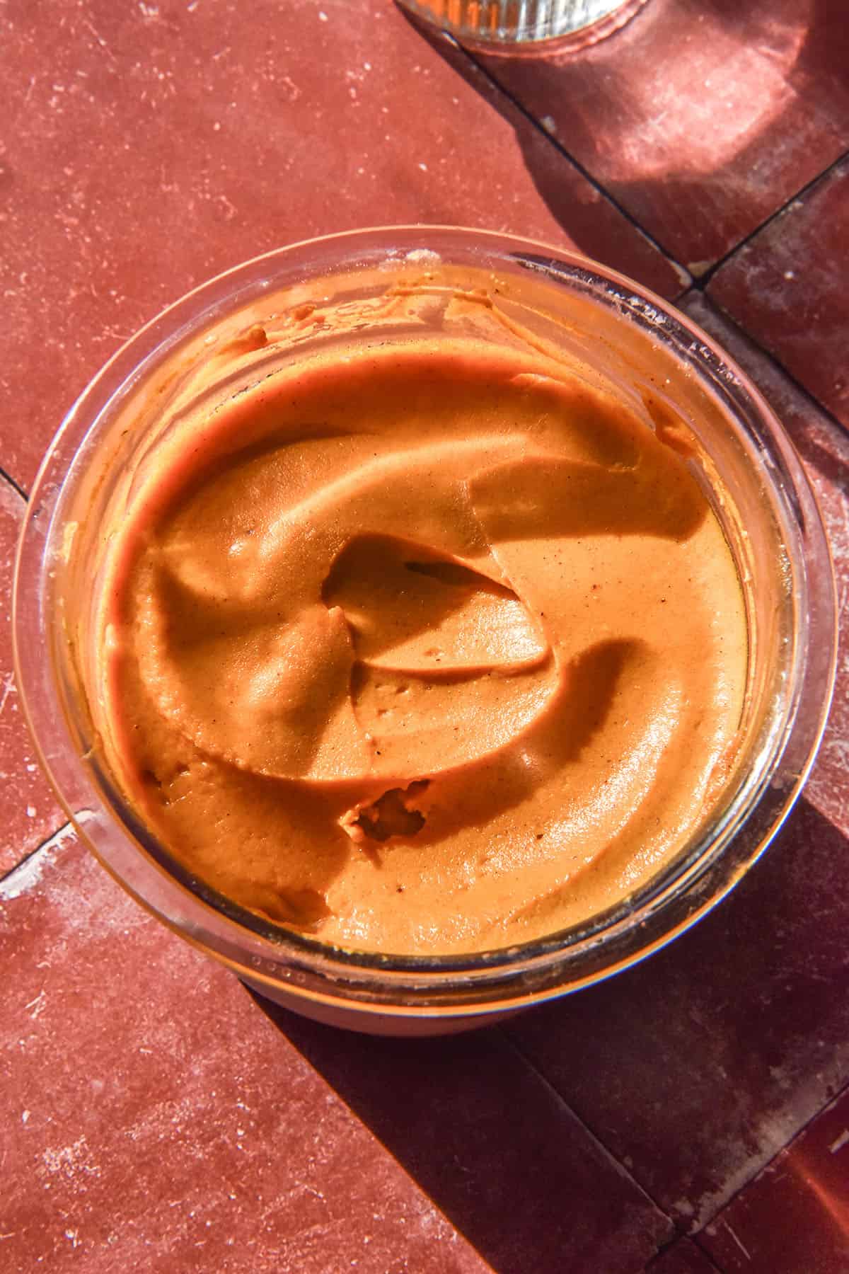 A sunlit aerial image of a tub of high protein pumpkin spice Ninja Creami on a terracotta tile backdrop