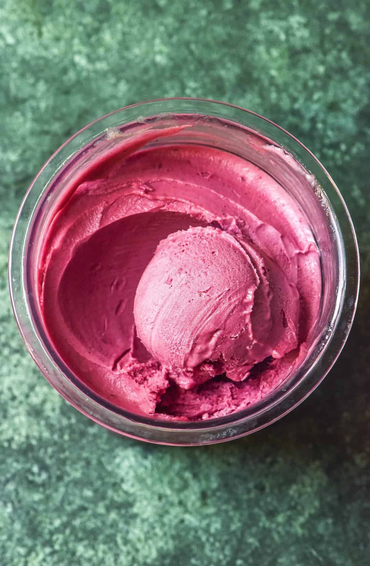 An aerial image of a tub of high protein Ninja Creami raspberry sorbet on an olive green backdrop