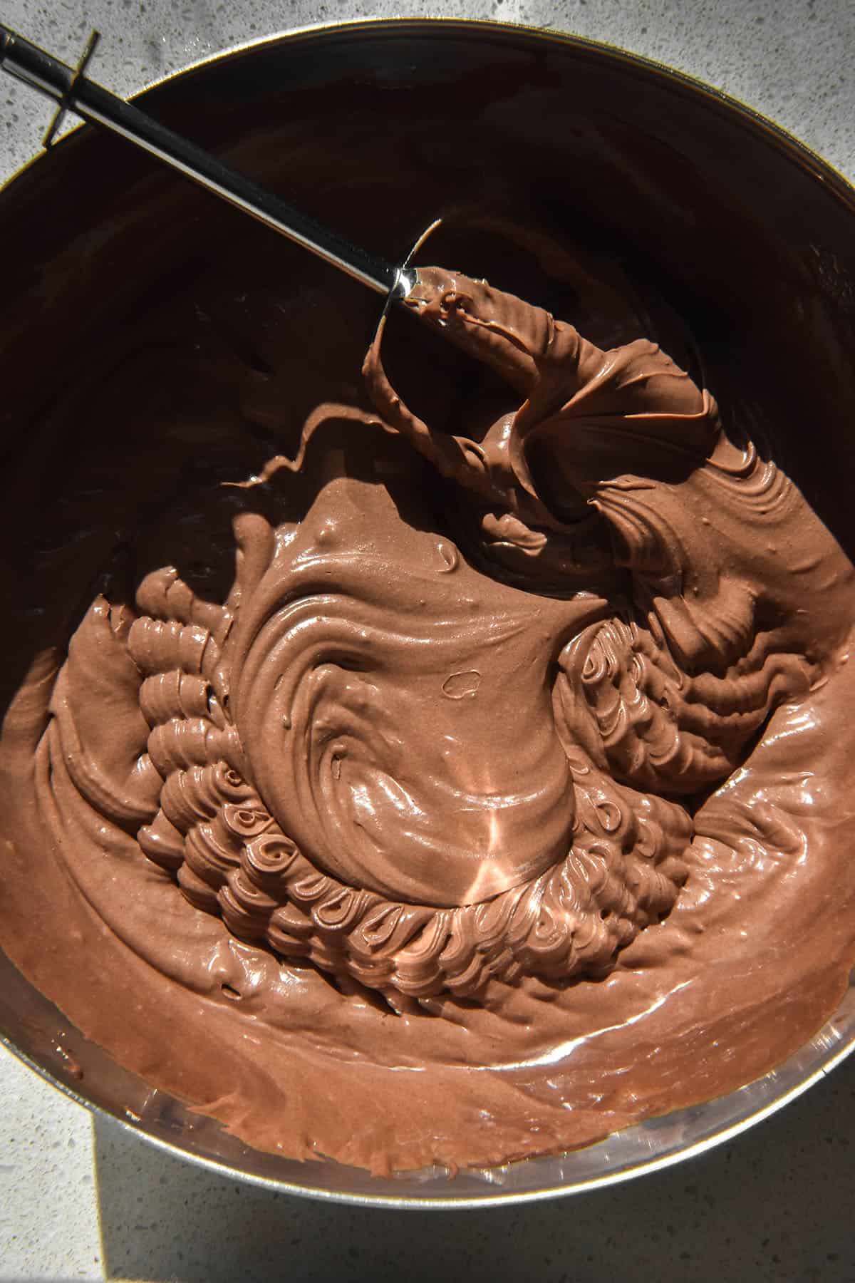 An aerial sunlit image of a bowl of lactose free chocolate mousse that is in the process of being whipped with stand beaters