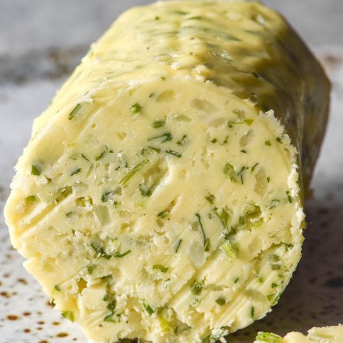 A side on image of a log of low FODMAP garlic butter on a white speckled ceramic plate against a white backdrop