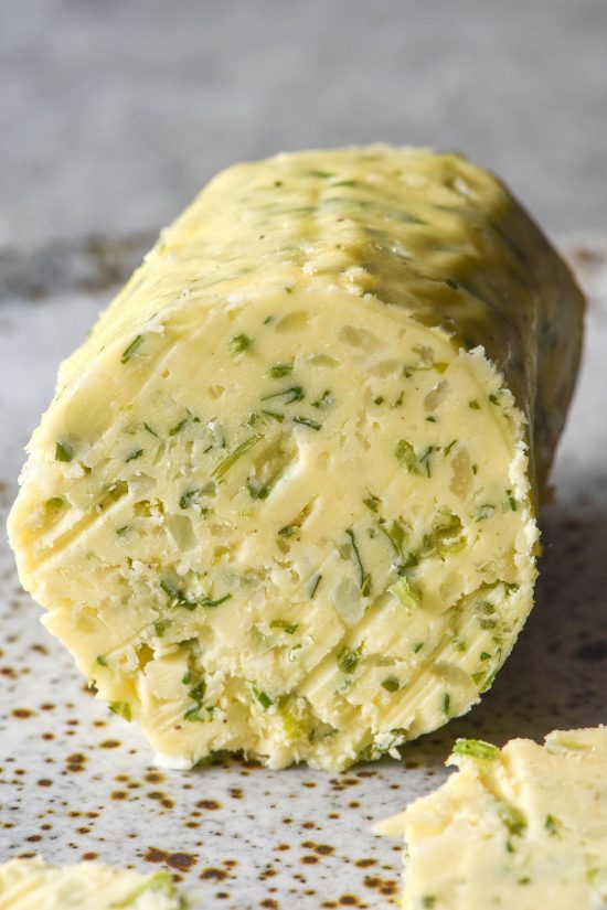 A side on image of a log of low FODMAP garlic butter on a white speckled ceramic plate against a white backdrop