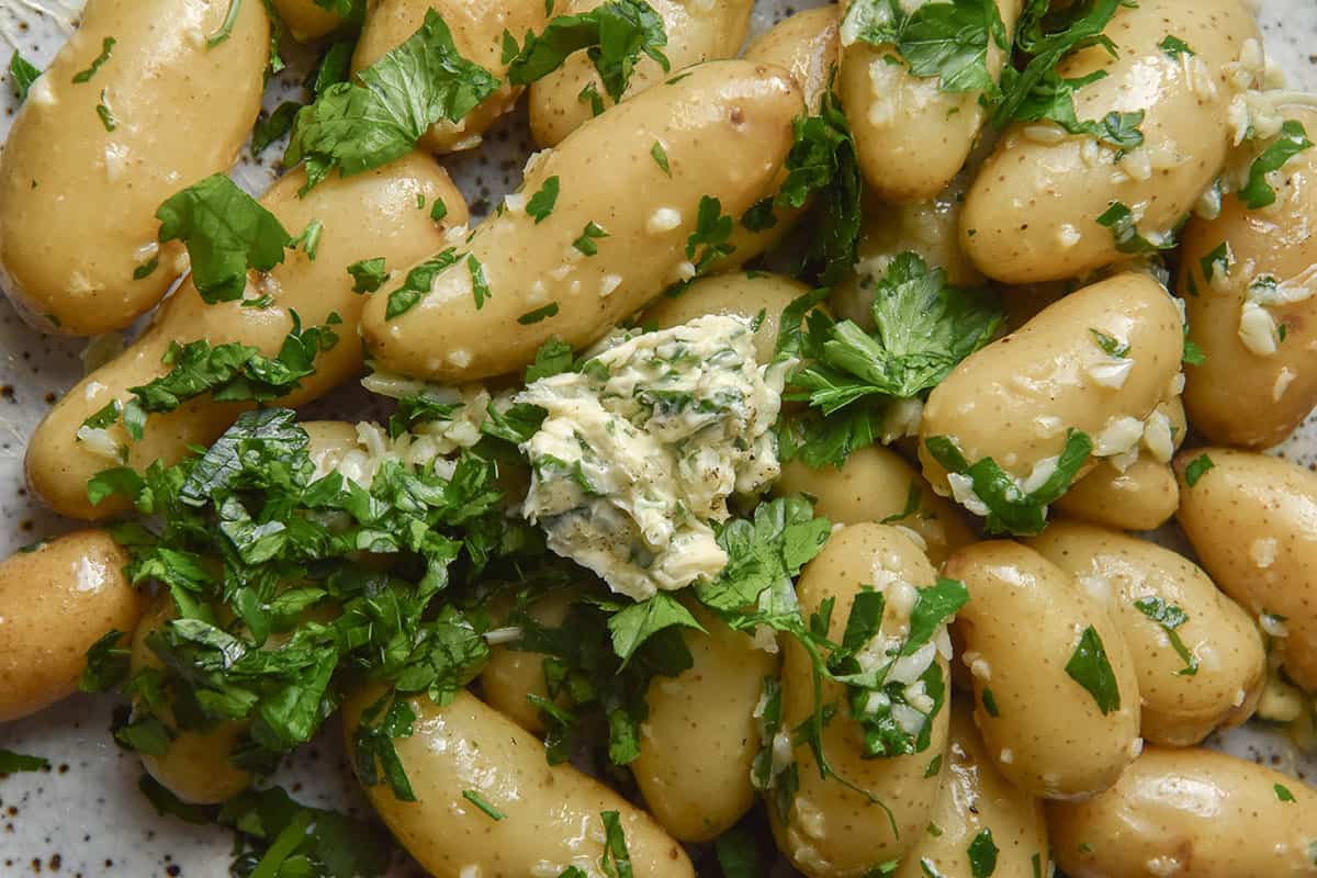 A close up aerial image of boiled kipfler potatoes smothered in low FODMAP garlic butter and finished with parsley