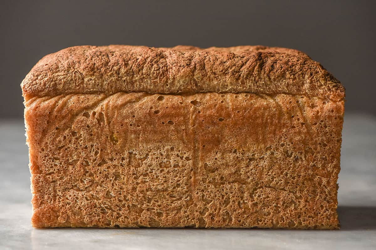 A side on image of a loaf of millet bread that sits atop a white marble table against a dark backdrop