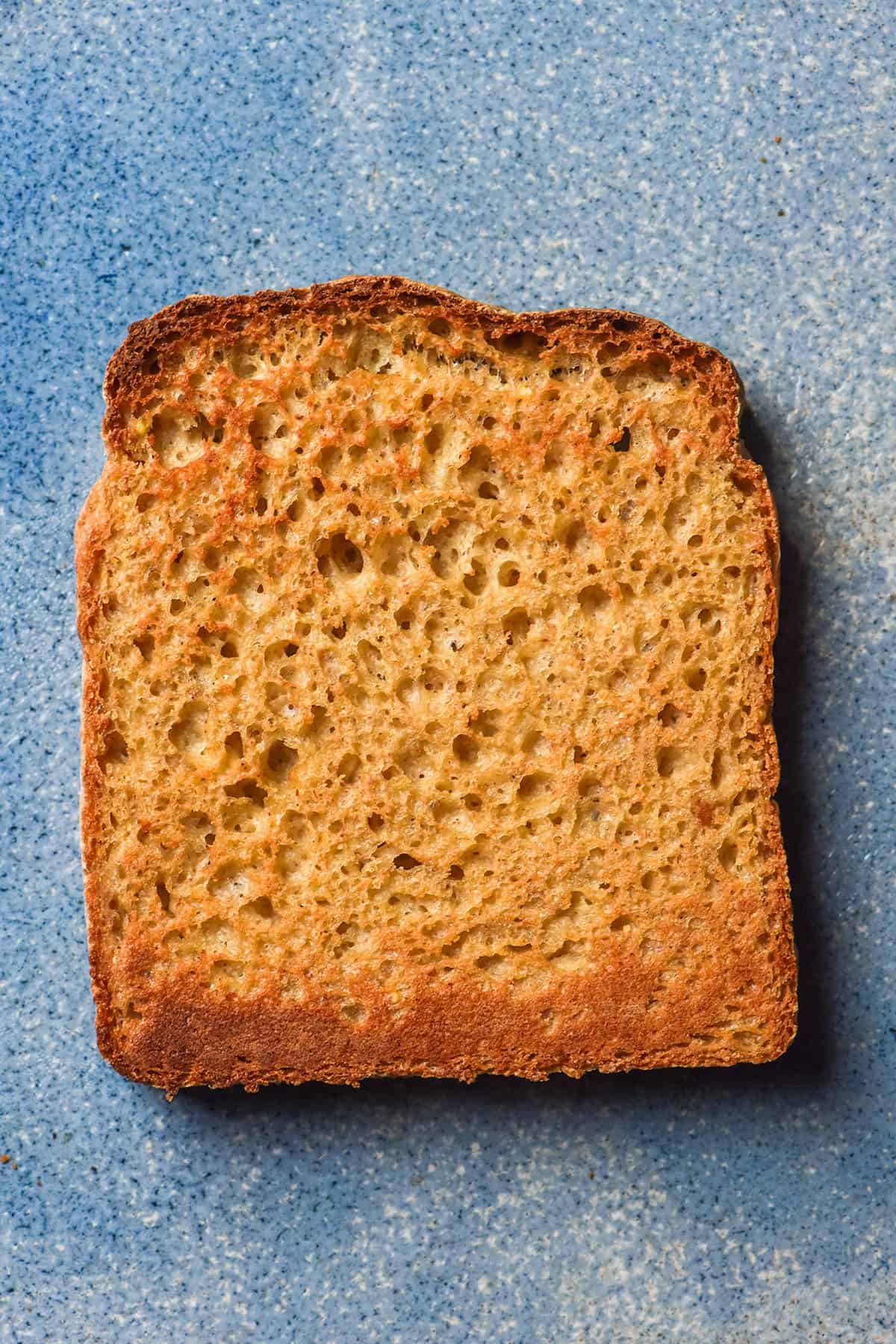 An aerial image of a slice of millet bread that has been toasted and sits atop a bright blue ceramic plate