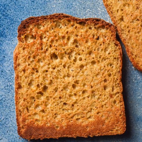 An aerial image of a slice of millet bread that has been toasted and sits atop a bright blue ceramic plate