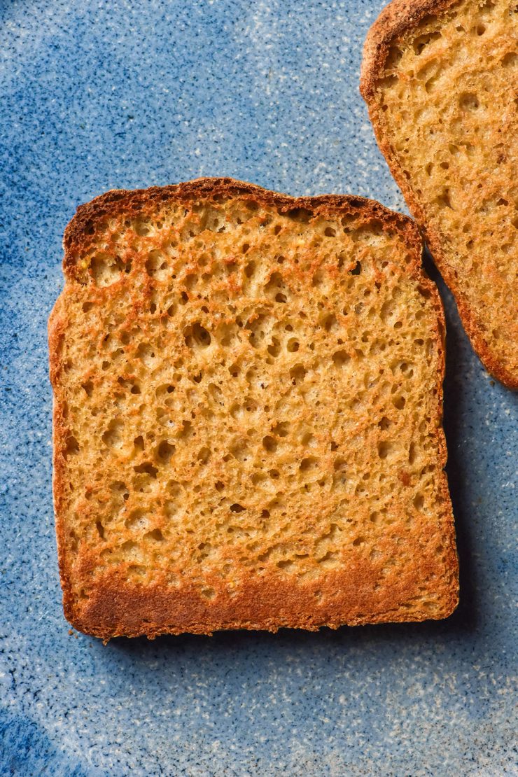 An aerial image of a slice of millet bread that has been toasted and sits atop a bright blue ceramic plate