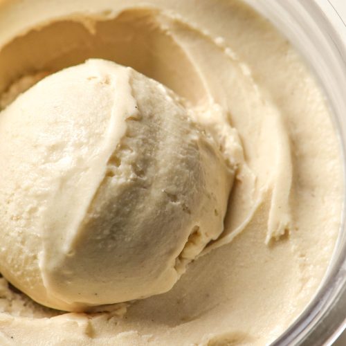 A close up aerial image of a tub of Ninja Creami banana ice cream. There is a scoop of creamy banana ice cream sitting atop the tub in the middle.