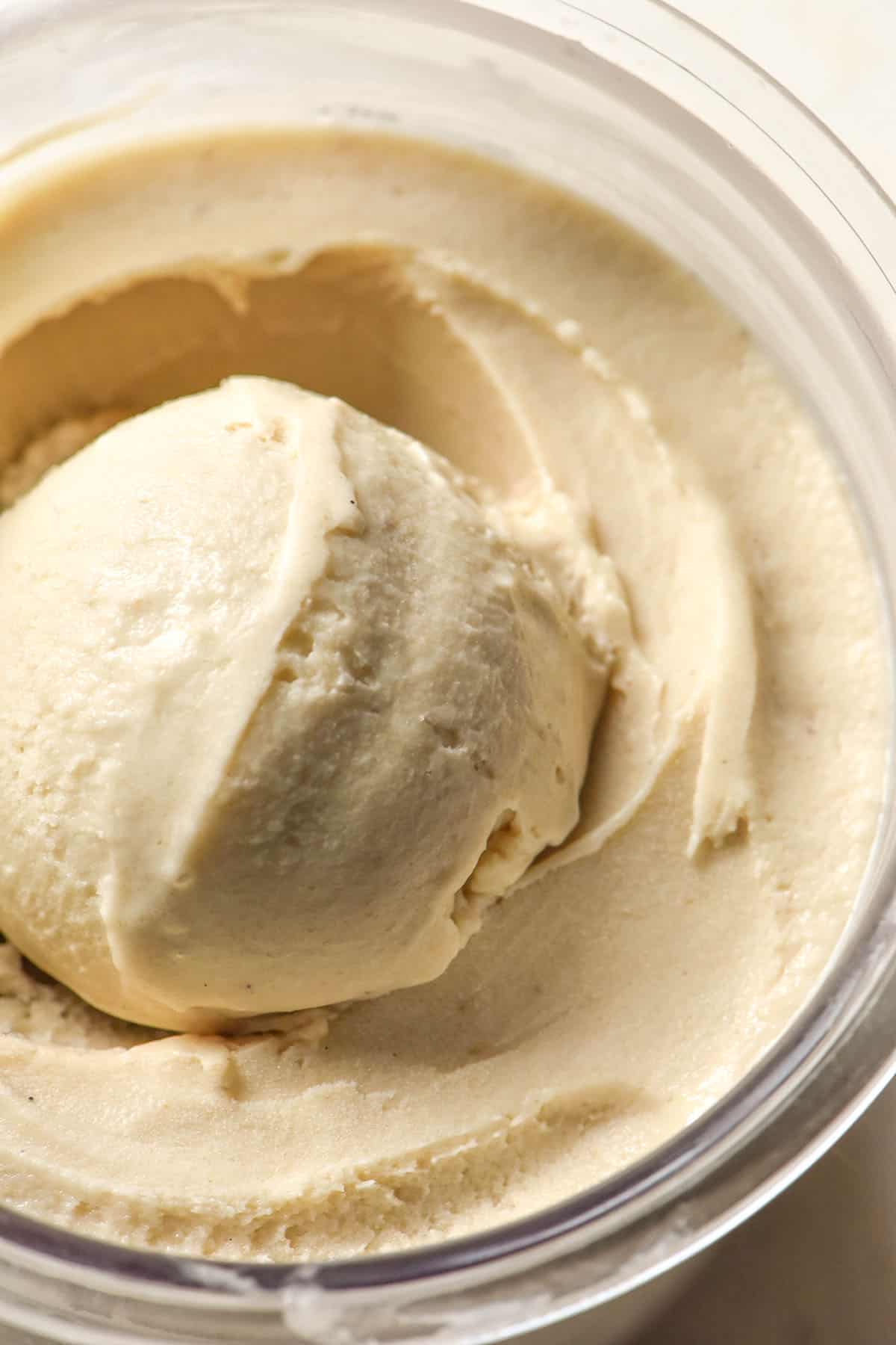 A close up aerial image of a tub of Ninja Creami banana ice cream. There is a scoop of creamy banana ice cream sitting atop the tub in the middle. 