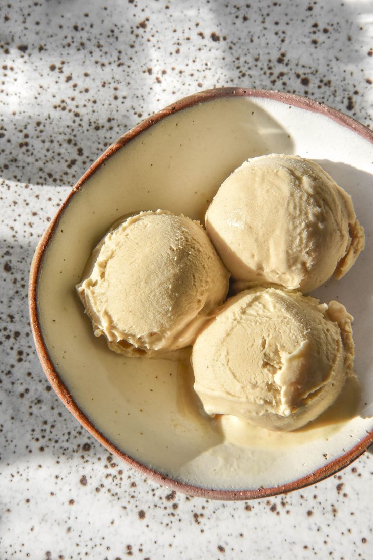 A brightly lit aerial image of three scoops of Ninja Creami banana ice cream in a small white ceramic bowl atop a white speckled ceramic plate