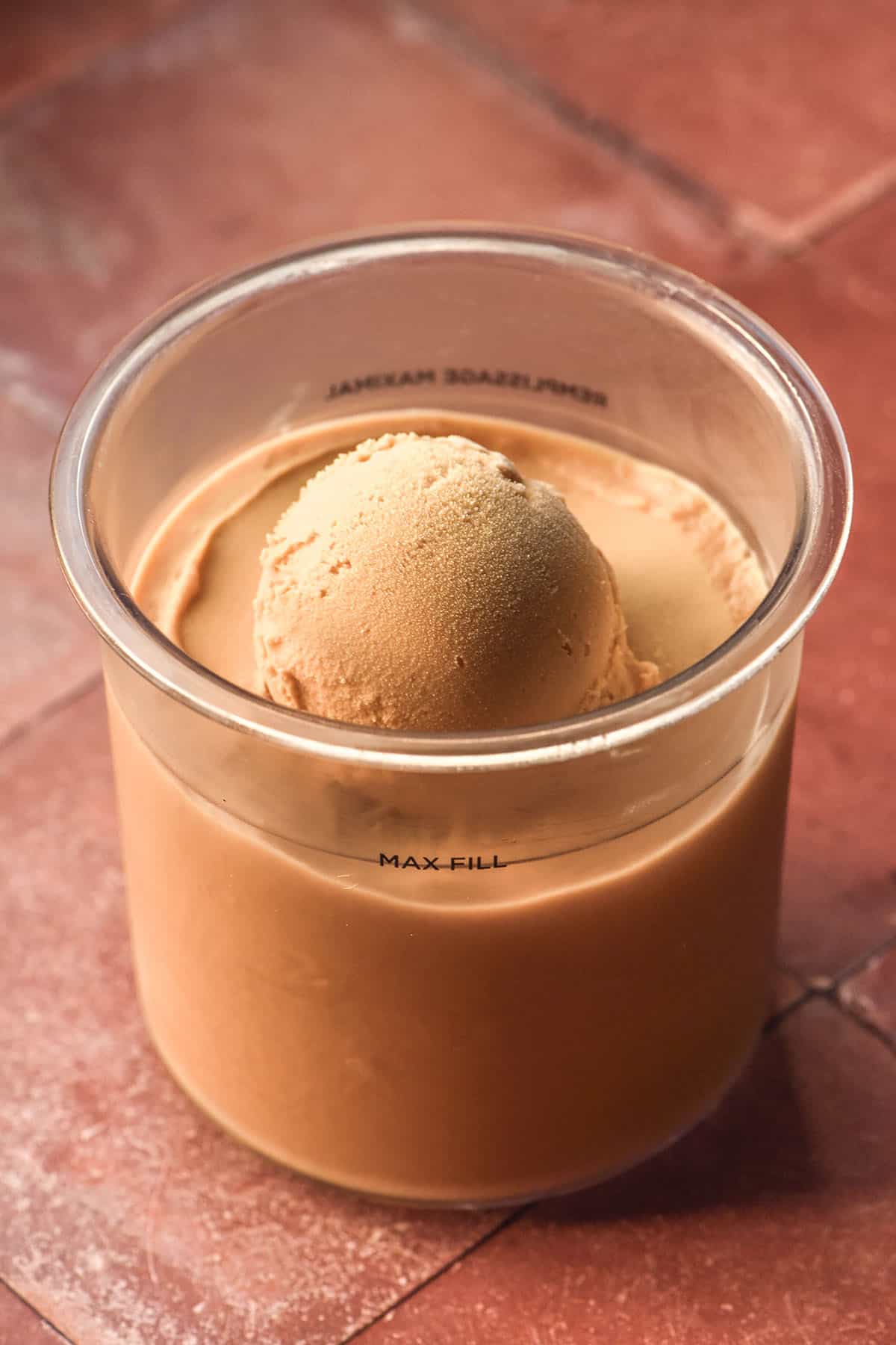 An image of a tub of Ninja Creami coffee ice cream on a terracotta tile backdrop. The tub has a scoop of ice cream perched in the centre.