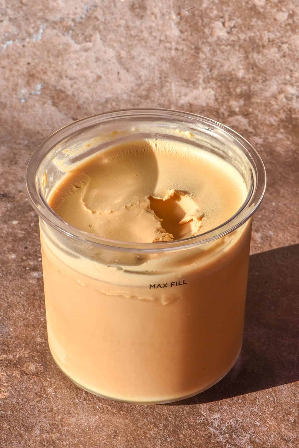 A sunlit image of a tub of Ninja Creami coffee ice cream on a light brown backdrop