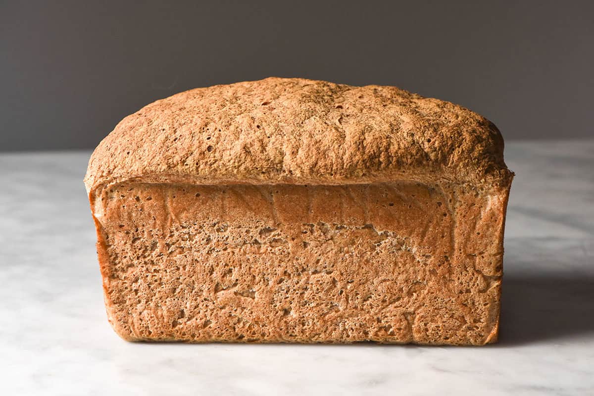 An image of a gluten free sorghum bread loaf atop a white marble table against a dark backdrop