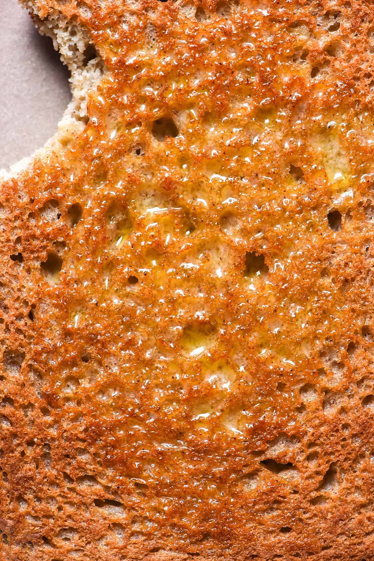 A close up macro image of a slice of sorghum bread toast slathered in butter. The piece of toast is golden brown and has a bite taken from the top left corner