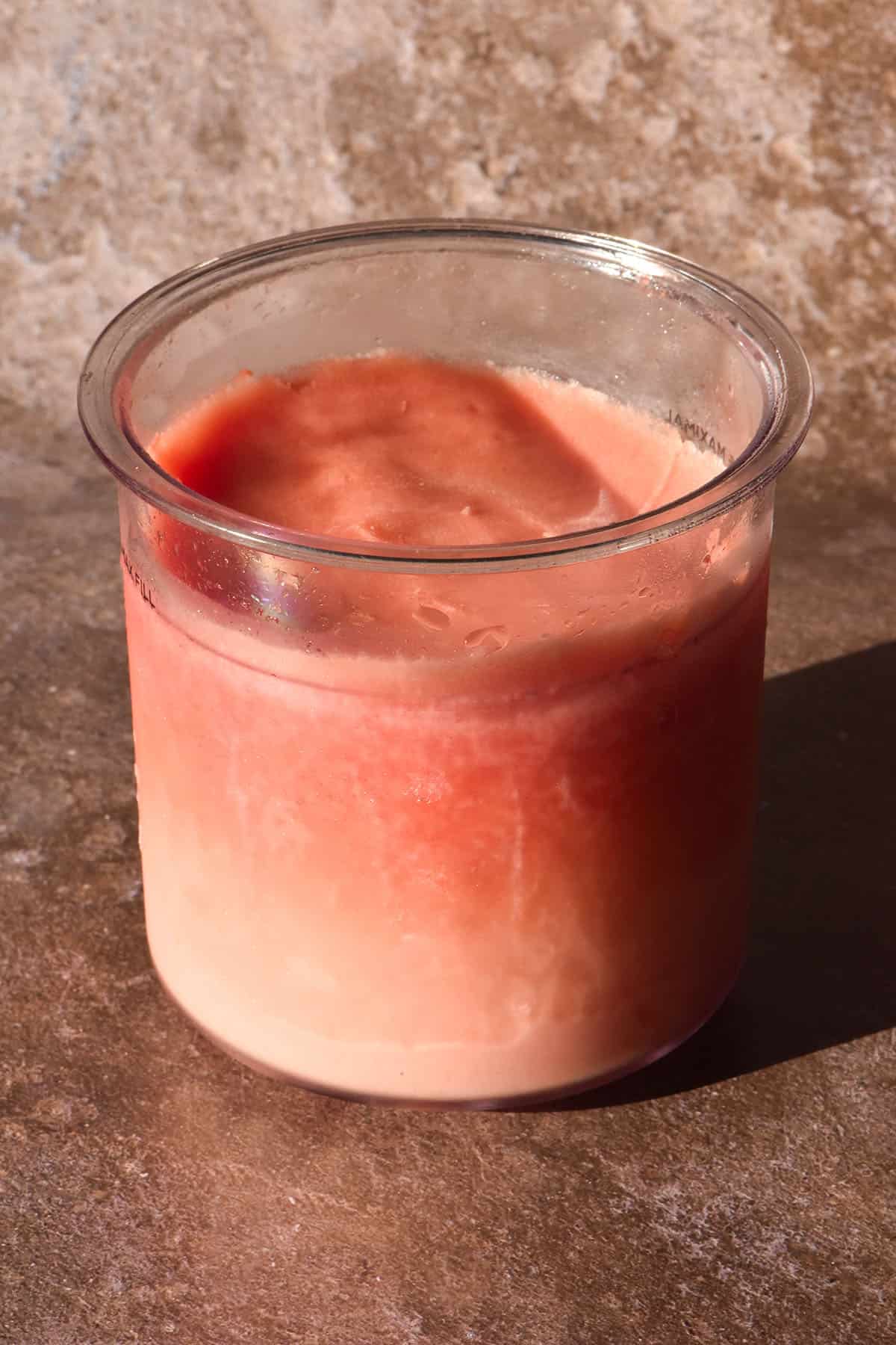 A brightly lit image of a tub of Ninja Creami watermelon sorbet against a light brown speckled backdrop