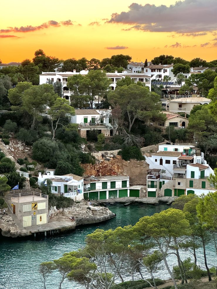 An image of the fishermen's houses and water at Cala Santanyi at sunset