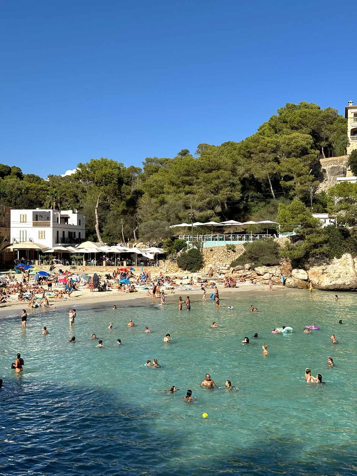 An image of Cala Santanyi on a sunny day with lots of people in the water