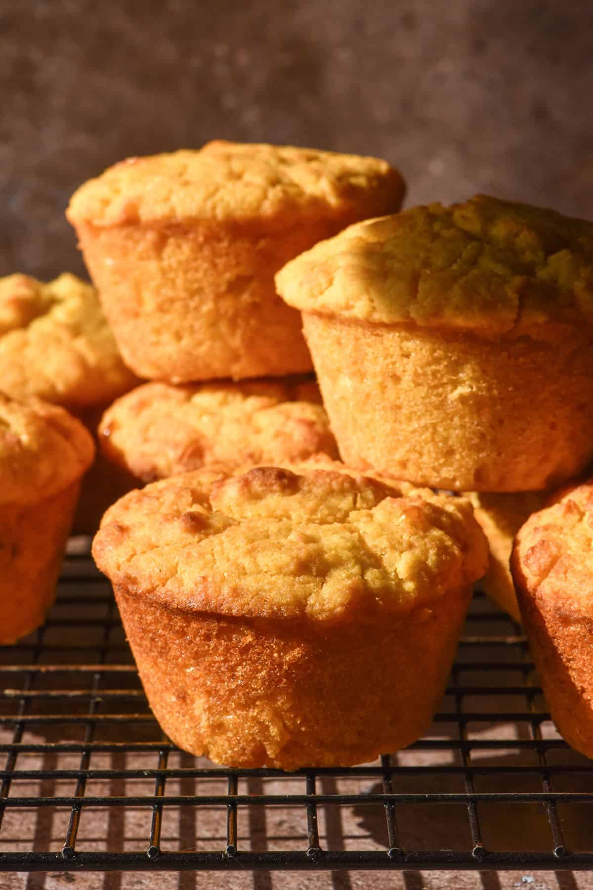 A brightly lit side on image of gluten free cornbread muffins on a cooling rack against a dark brown backdrop