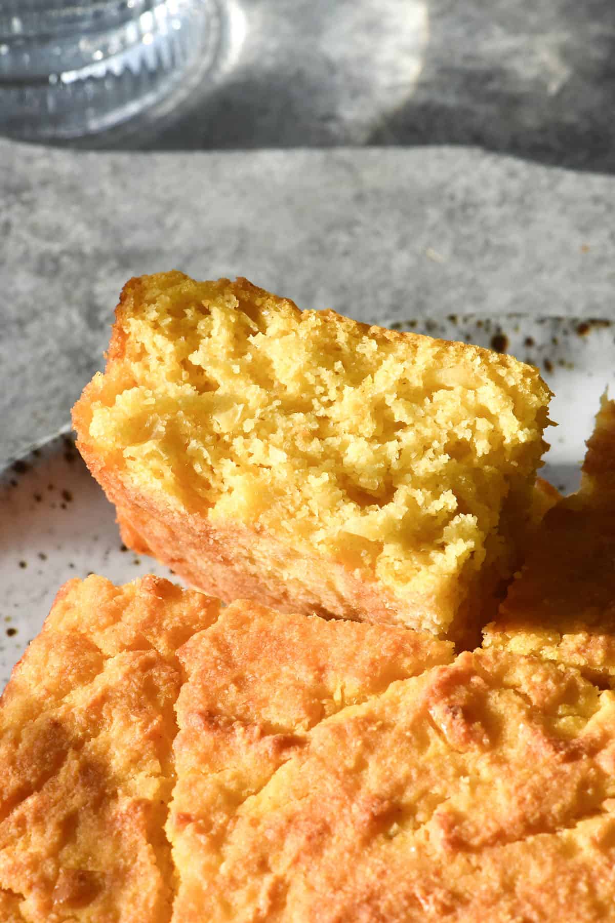 An side on image of a square gluten free cornbread on a white speckled ceramic plate