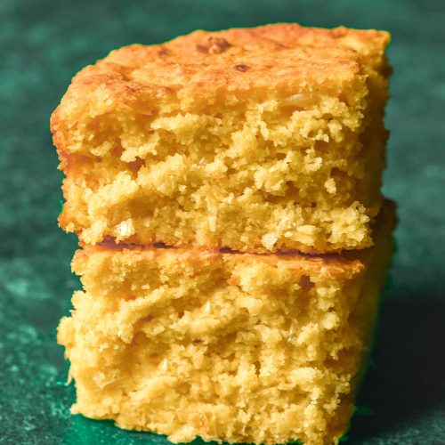 A side on image of two slices of gluten free vegan cornbread stacked on top of each other against an olive green backdrop