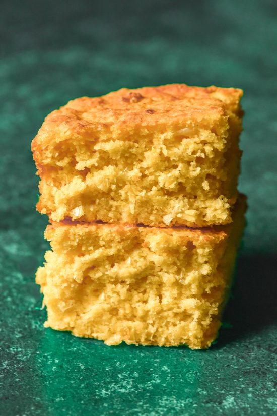 A side on image of two slices of gluten free vegan cornbread stacked on top of each other against an olive green backdrop