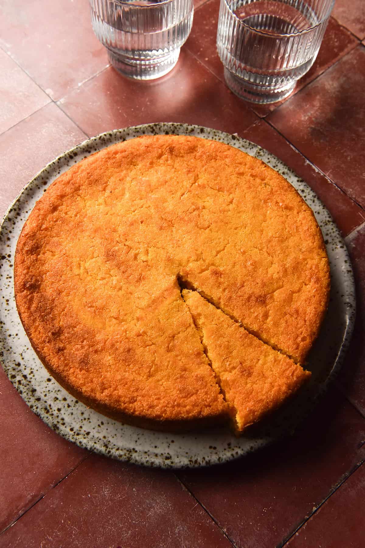 An aerial image of a round gluten free vegan on a white speckled ceramic plate atop a terracotta tile backdrop