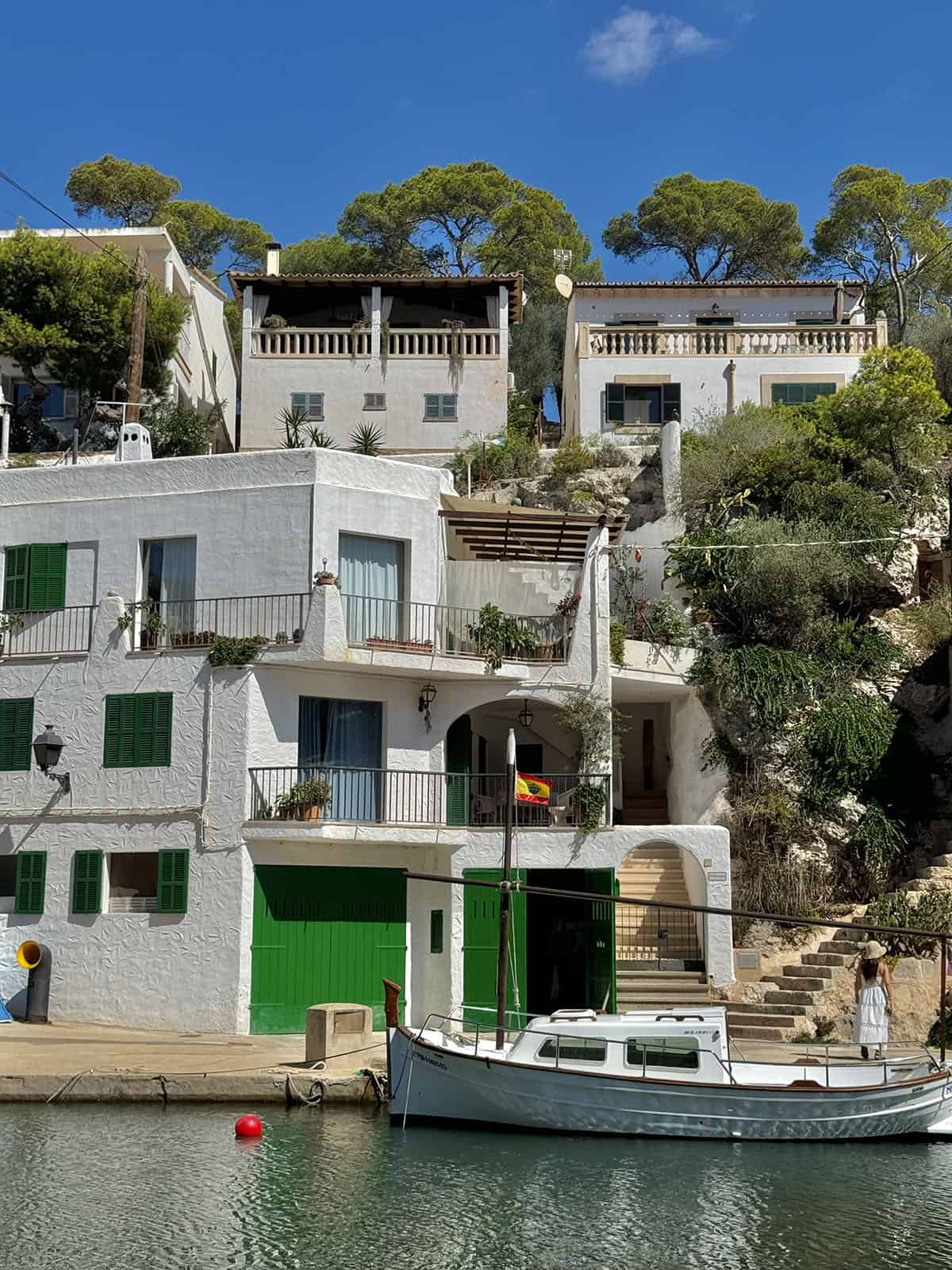 An image of the houses and water at Cala Figuera, Mallorca. The houses are set against a sunny sky and a boat sits in the water in front of the house.