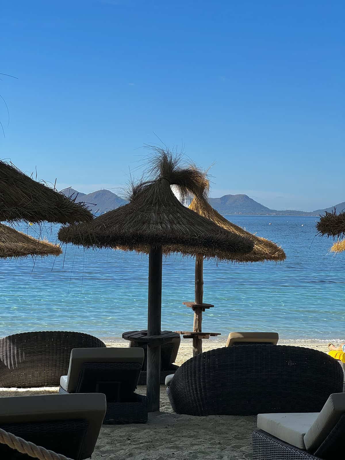 An image of the thatched beach umbrellas and sun chairs set against the bright blue water at Cala Formentor