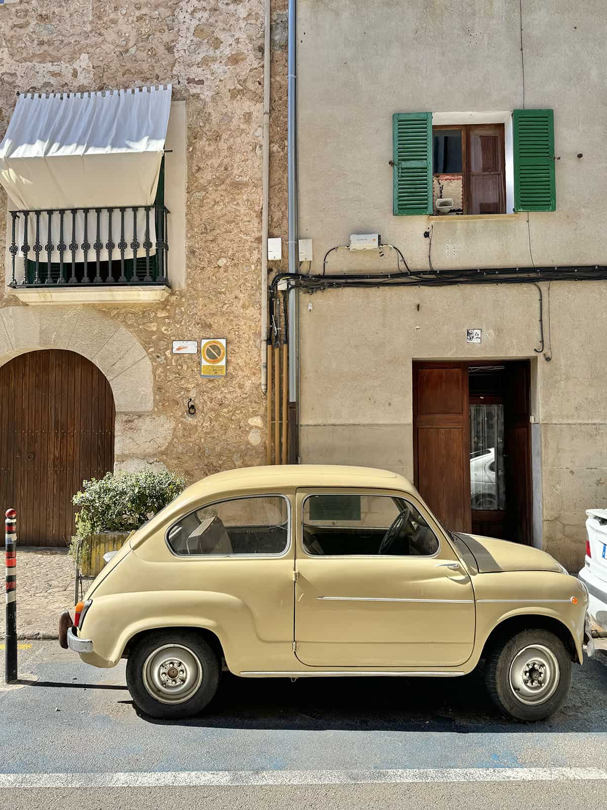 An image of an old pale yellow car parked in front of Mallorcan buildings in Soller, Mallorca