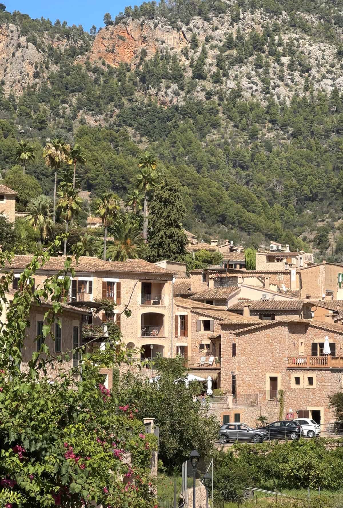 The view of Fornalutx as seen from the walk from Soller. Lush green surrounds the stone houses set against a mountainous backdrop and a blue sky