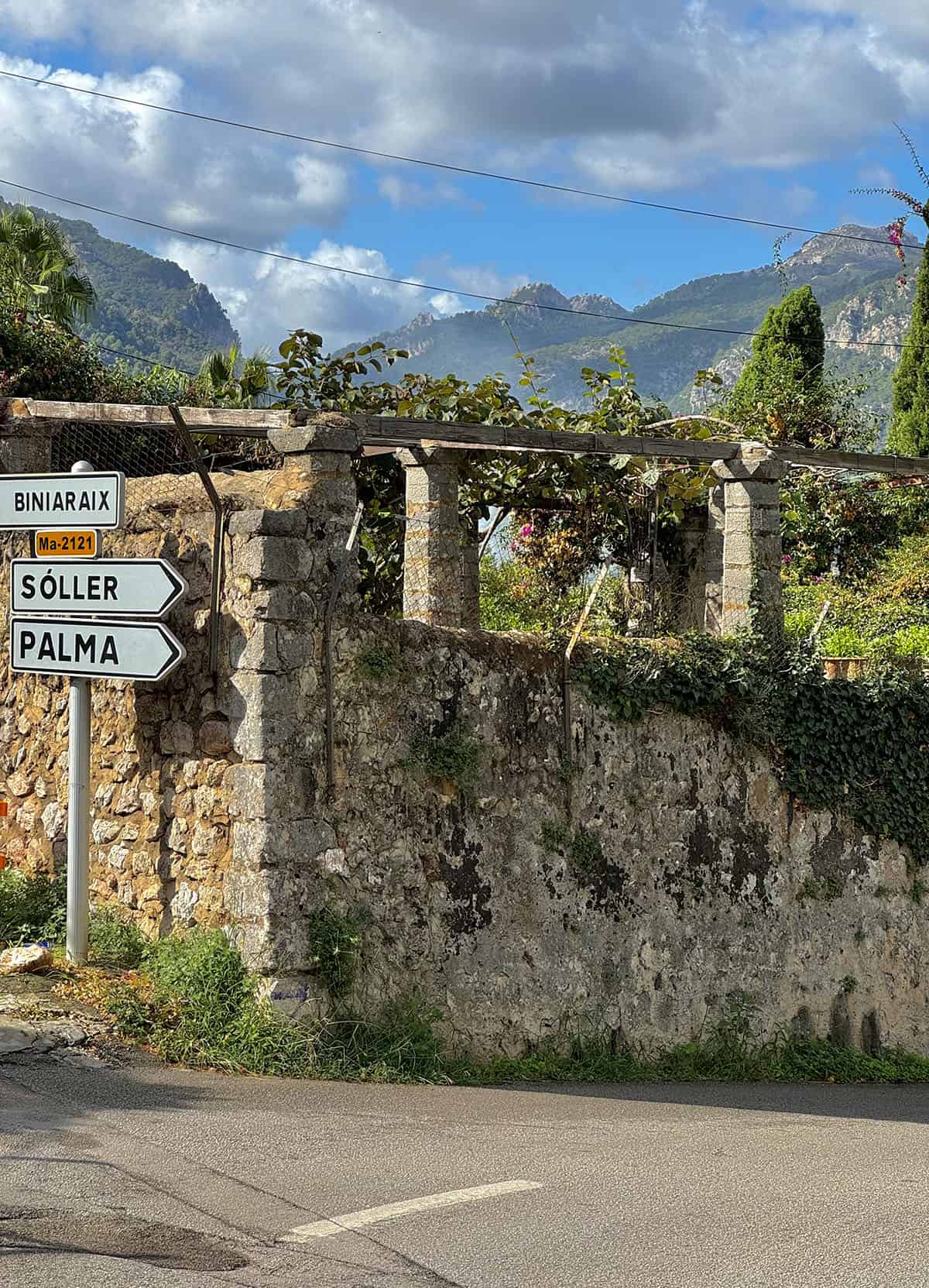 A road in Mallorca between Soller and Fornalutx. Blue skies, a rustic fence and town signs are set in front of a mountainous backdrop