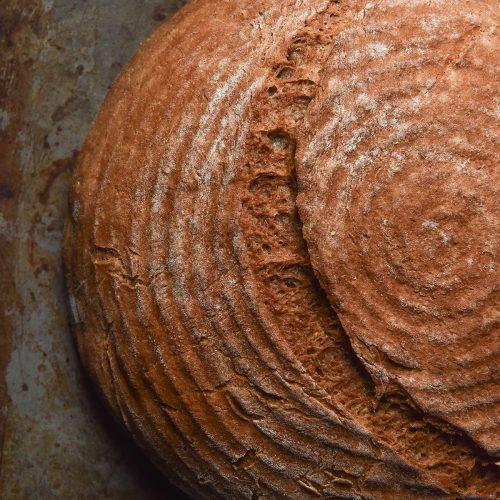 A close up aerial image of a boule of gluten free buckwheat bread on a dark steel backdrop