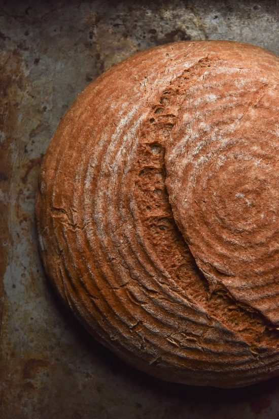 A close up aerial image of a boule of gluten free buckwheat bread on a dark steel backdrop