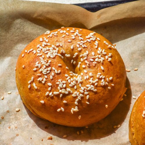 A sunlit image of gluten free pumpkin bagels topped with sesame seeds on a baking tray