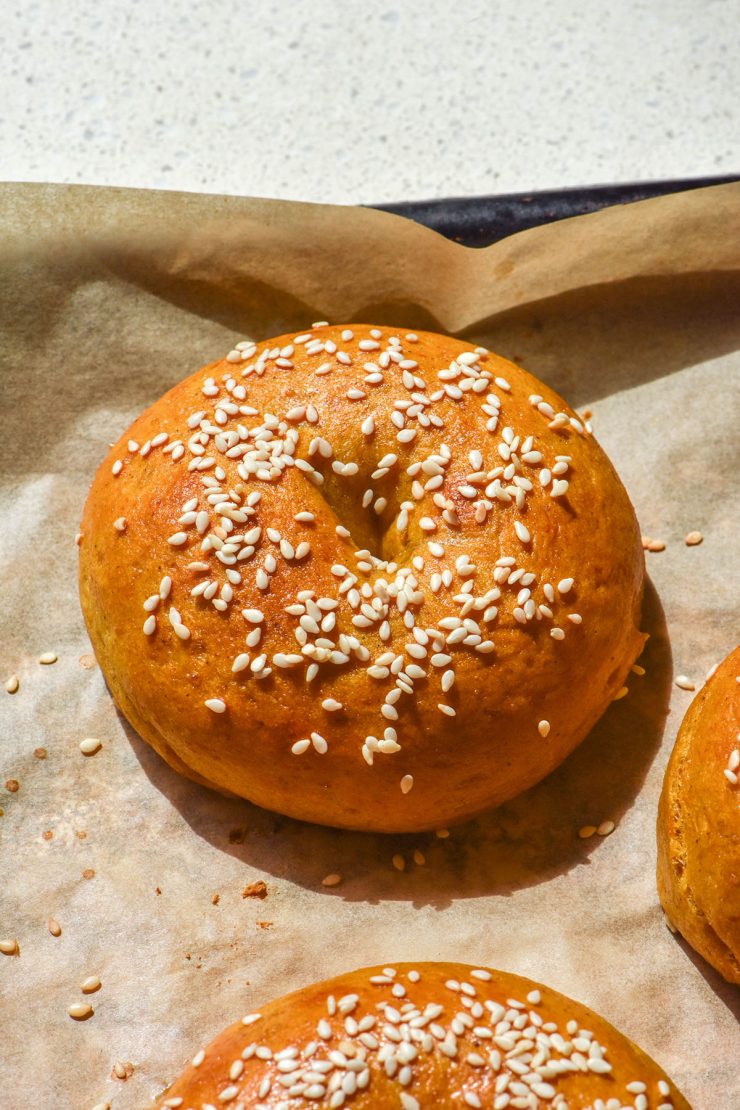 A sunlit image of gluten free pumpkin bagels topped with sesame seeds on a baking tray